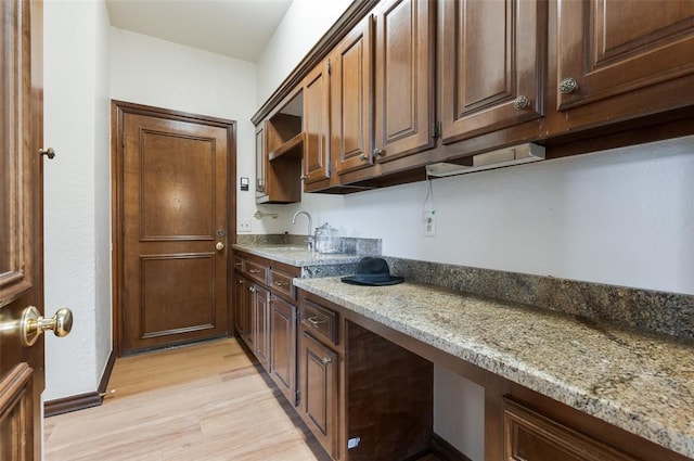 kitchen featuring open shelves, light wood finished floors, dark brown cabinets, and light stone countertops