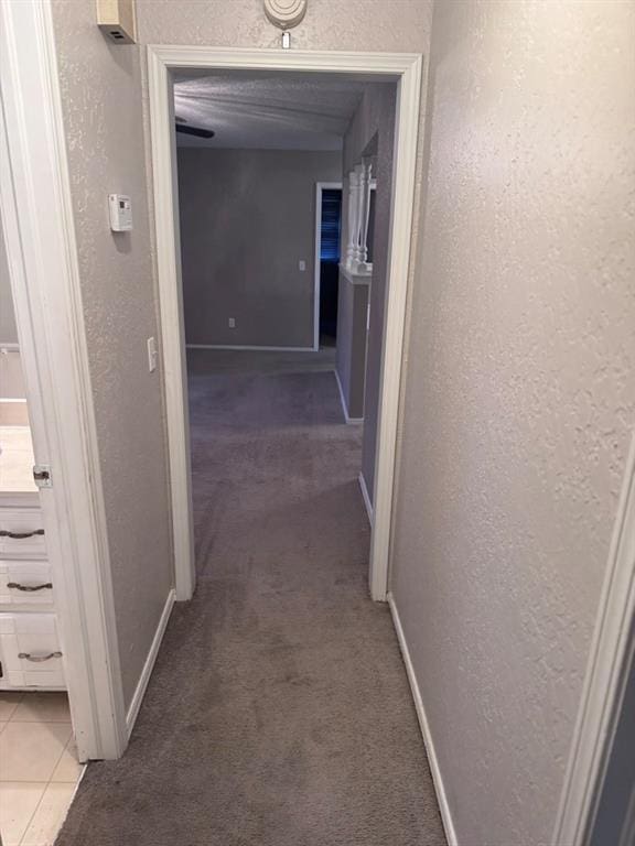 corridor with light colored carpet, a textured wall, baseboards, and light tile patterned flooring