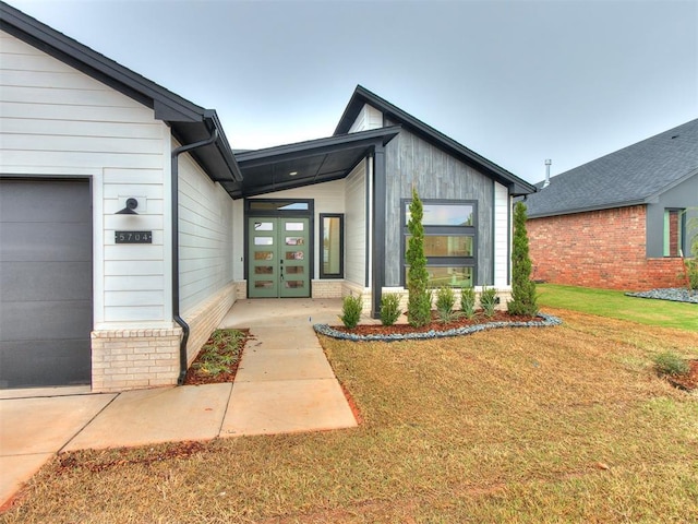 property entrance featuring a garage, brick siding, a lawn, and french doors