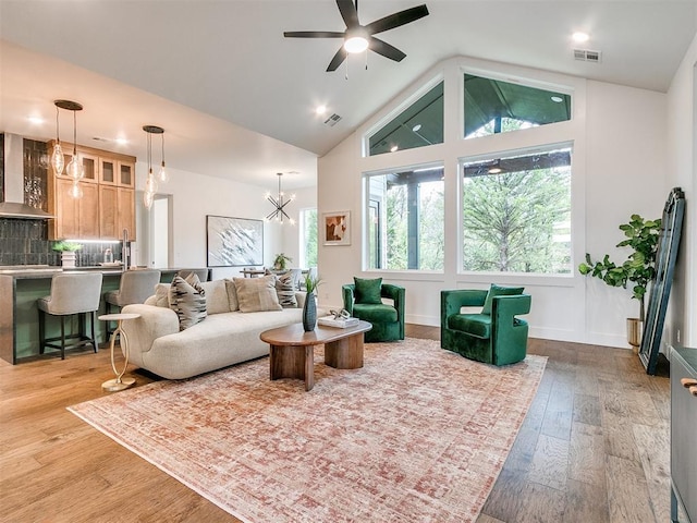 living room with baseboards, visible vents, lofted ceiling, light wood-style floors, and ceiling fan with notable chandelier