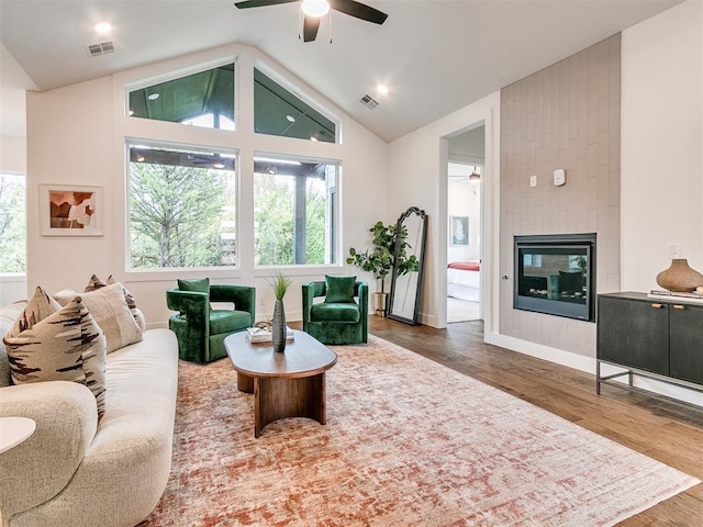 living area with a ceiling fan, visible vents, a fireplace, and wood finished floors