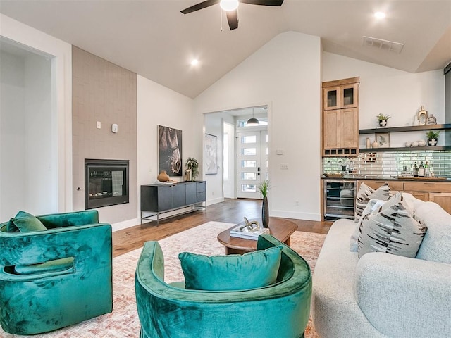 living room with wine cooler, wood finished floors, visible vents, baseboards, and a glass covered fireplace