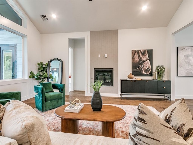 living area with a large fireplace, wood finished floors, lofted ceiling, and visible vents