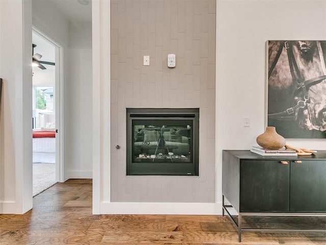 room details with a glass covered fireplace, wood finished floors, a ceiling fan, and baseboards