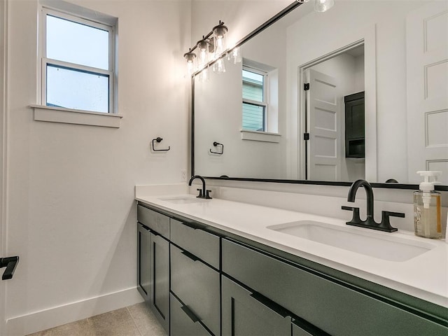 full bathroom with double vanity, tile patterned flooring, a sink, and baseboards