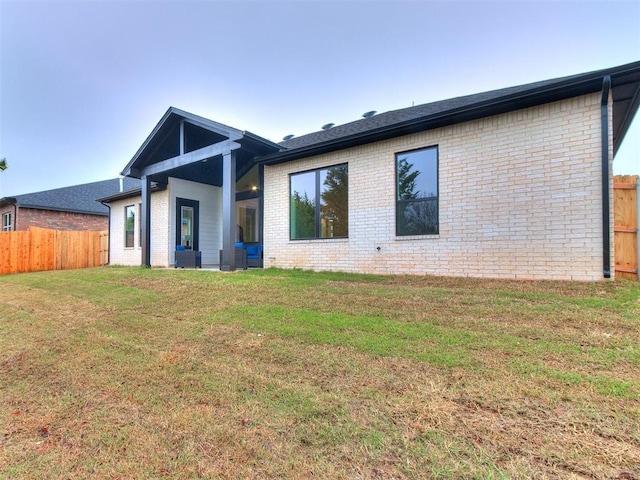 rear view of house with central AC unit, fence, a lawn, and brick siding