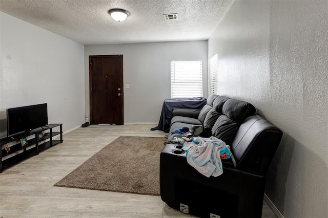 living room with visible vents, a textured ceiling, light wood finished floors, and baseboards