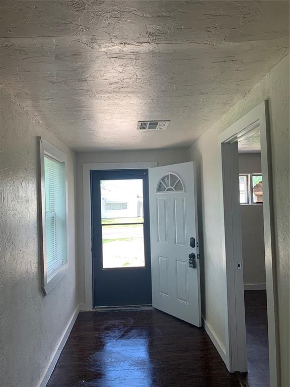 doorway to outside featuring dark wood-style floors, a healthy amount of sunlight, visible vents, and a textured wall