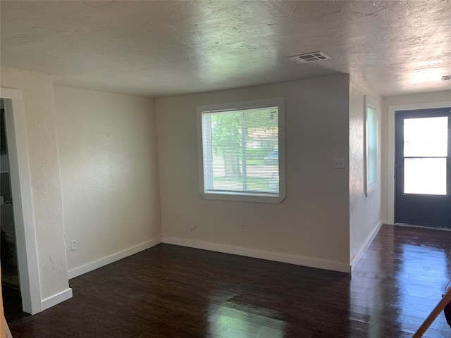 unfurnished room featuring a healthy amount of sunlight, visible vents, baseboards, and wood finished floors