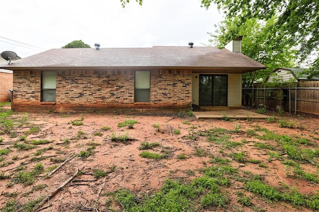 rear view of house with brick siding, fence, a chimney, and a patio
