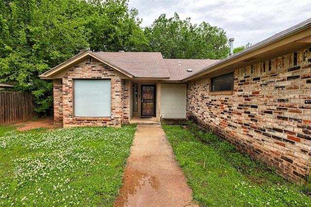 view of front of house with brick siding, fence, a front yard, and roof with shingles