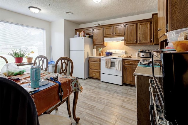 kitchen with brown cabinets, white appliances, light countertops, a textured ceiling, and under cabinet range hood
