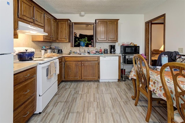 kitchen featuring a textured ceiling, a sink, light countertops, under cabinet range hood, and white appliances