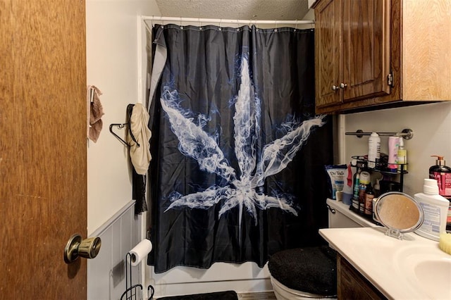 bathroom featuring a shower with curtain, a textured ceiling, a wainscoted wall, vanity, and toilet
