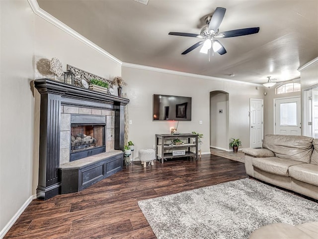 living room with arched walkways, crown molding, a tile fireplace, and wood finished floors