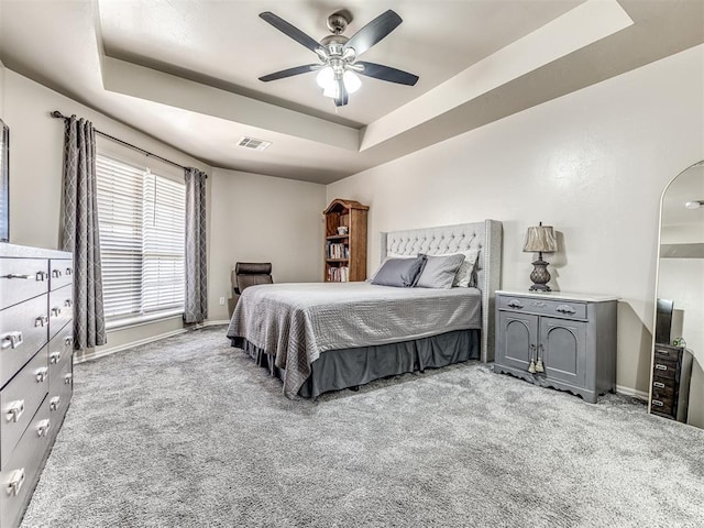 carpeted bedroom with baseboards, visible vents, a raised ceiling, and a ceiling fan