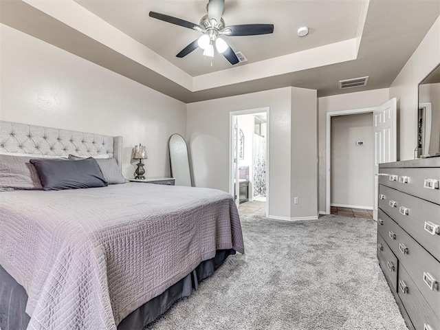 carpeted bedroom with a ceiling fan, a raised ceiling, visible vents, and connected bathroom