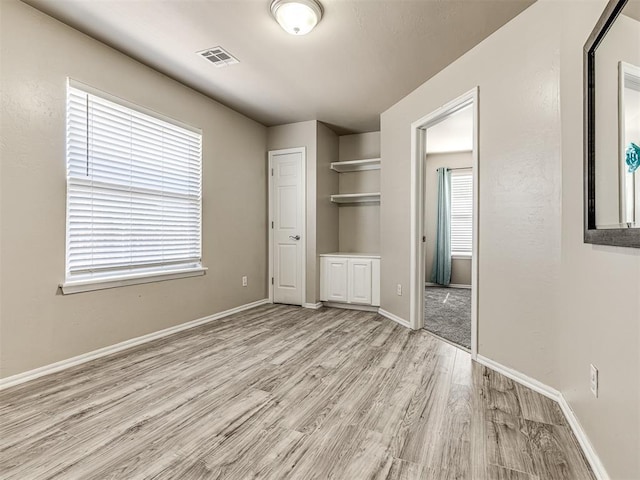 unfurnished bedroom featuring ensuite bathroom, light wood-style flooring, visible vents, and baseboards