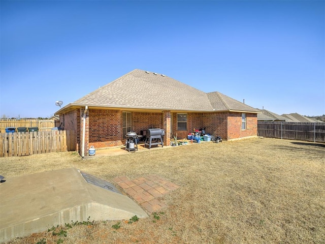 rear view of house featuring a shingled roof, brick siding, a patio, and a fenced backyard