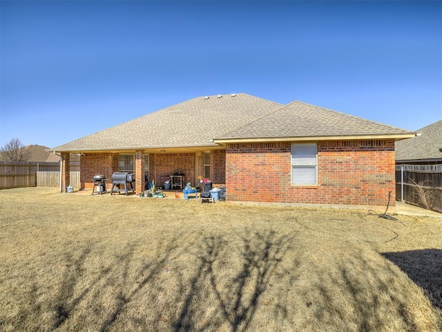 back of property with a yard, brick siding, a shingled roof, and fence