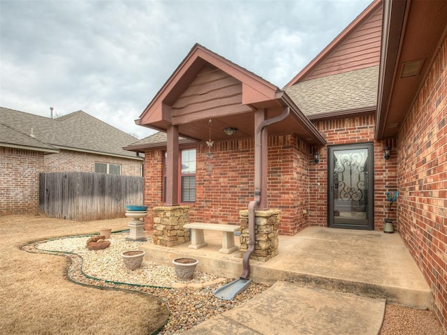 entrance to property with fence, brick siding, and roof with shingles