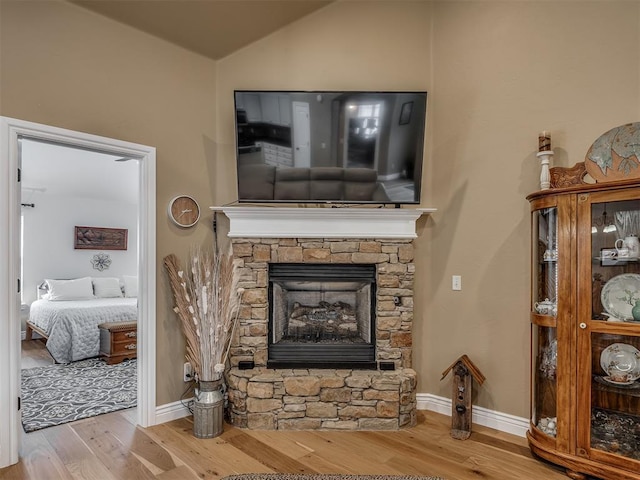 living area with a fireplace, vaulted ceiling, wood finished floors, and baseboards