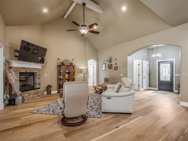 living area featuring ceiling fan with notable chandelier, a fireplace, light wood-style floors, arched walkways, and high vaulted ceiling