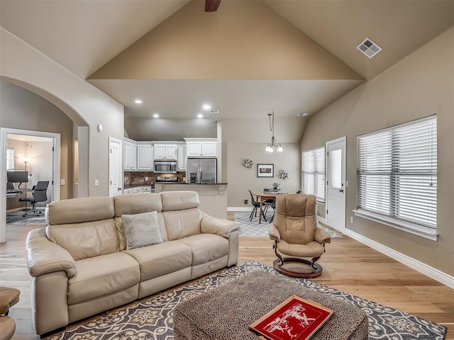 living area with light wood-type flooring, visible vents, high vaulted ceiling, arched walkways, and baseboards