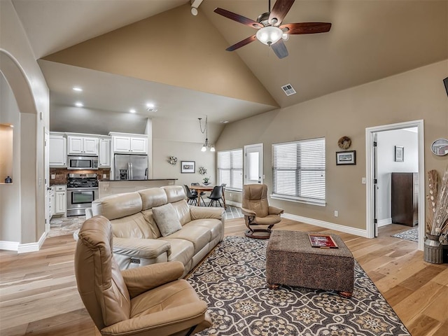 living area with visible vents, baseboards, ceiling fan, light wood-style floors, and high vaulted ceiling