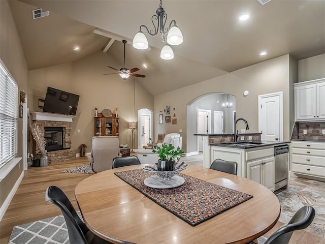 dining space featuring visible vents, ceiling fan with notable chandelier, arched walkways, a stone fireplace, and light wood finished floors