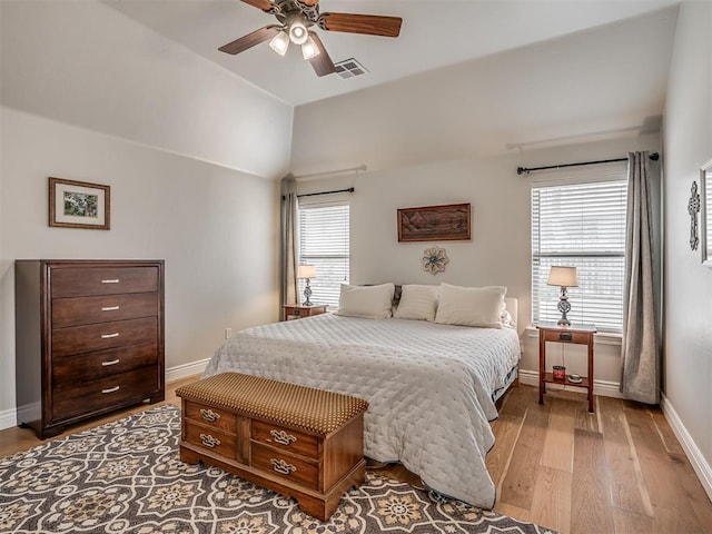 bedroom with a ceiling fan, wood finished floors, visible vents, baseboards, and vaulted ceiling