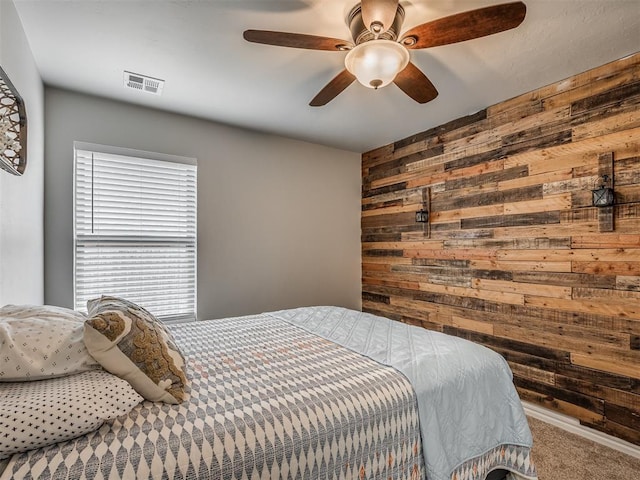 carpeted bedroom featuring visible vents, wood walls, and a ceiling fan