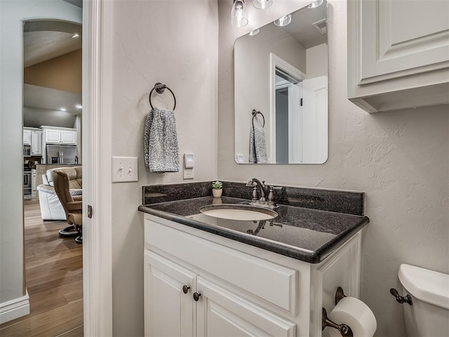 bathroom featuring vanity, wood finished floors, visible vents, toilet, and a textured wall