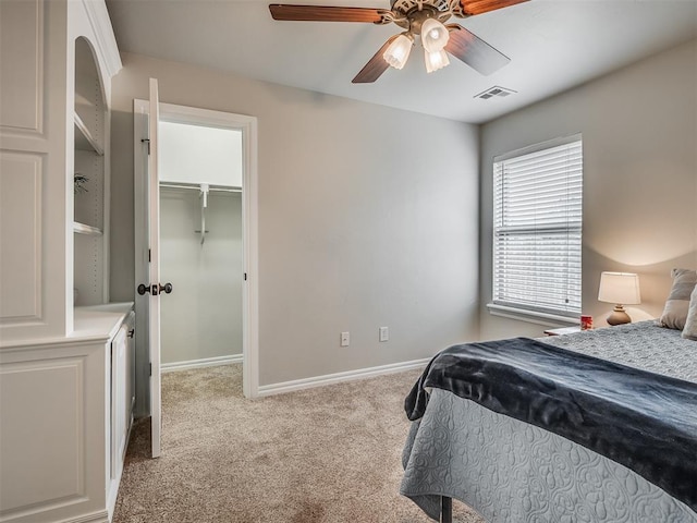 carpeted bedroom with a walk in closet, baseboards, visible vents, and a ceiling fan