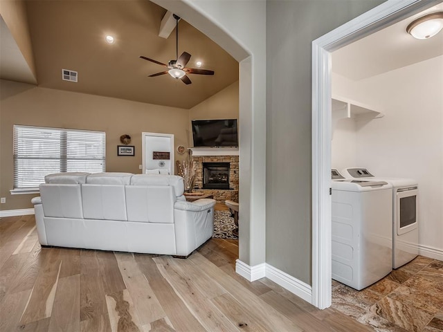 living area featuring visible vents, ceiling fan, light wood-type flooring, lofted ceiling, and a stone fireplace