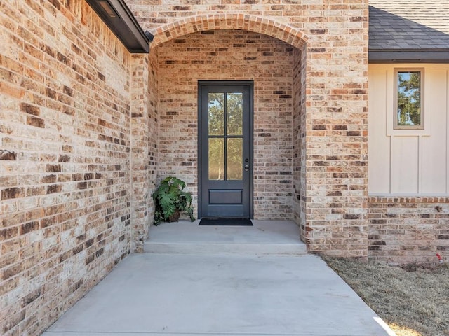 entrance to property featuring a shingled roof, board and batten siding, and brick siding