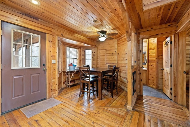 dining room featuring wooden walls, visible vents, light wood-type flooring, wooden ceiling, and a ceiling fan