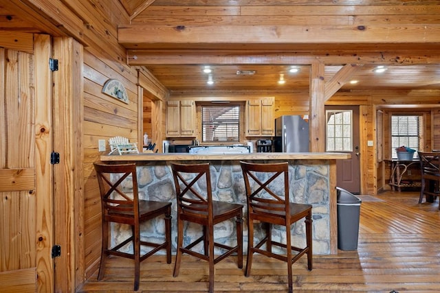 kitchen featuring a peninsula, freestanding refrigerator, light countertops, wood-type flooring, and a kitchen breakfast bar