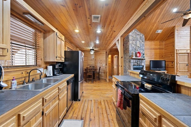 kitchen featuring visible vents, a sink, stainless steel appliances, wood walls, and ceiling fan