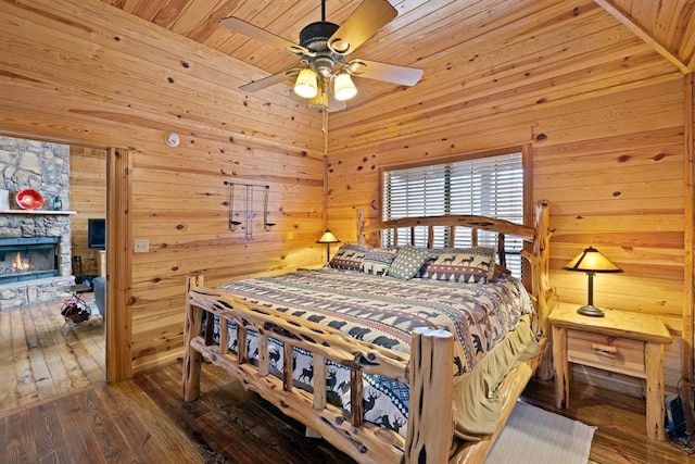 bedroom featuring hardwood / wood-style floors, wooden walls, a ceiling fan, a fireplace, and wooden ceiling