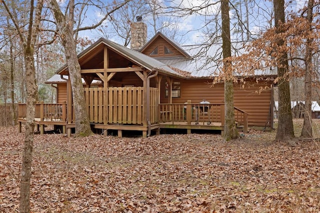 exterior space with log veneer siding, metal roof, a deck, and a chimney