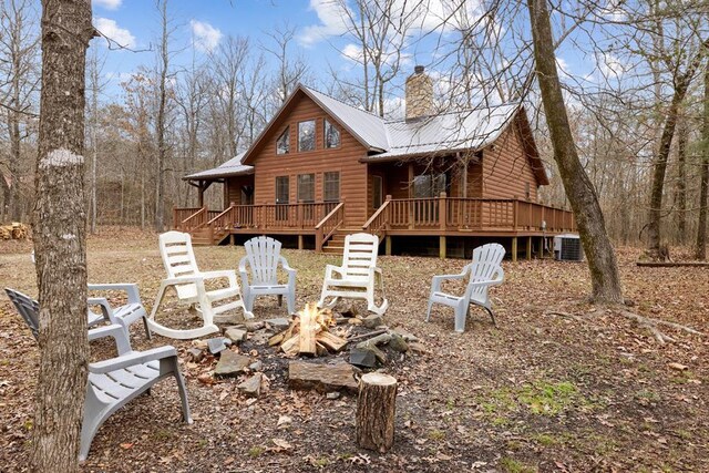 back of house featuring faux log siding, a fire pit, central air condition unit, a chimney, and a deck