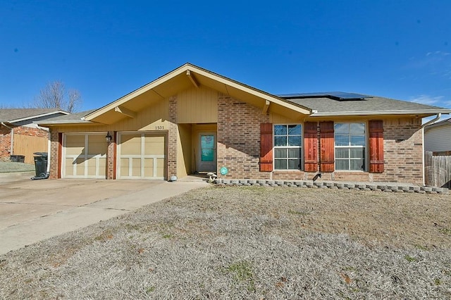 view of front facade with a garage, brick siding, fence, concrete driveway, and roof mounted solar panels