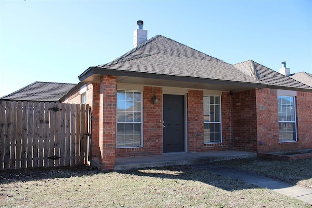 view of front of home featuring roof with shingles, brick siding, a chimney, and fence