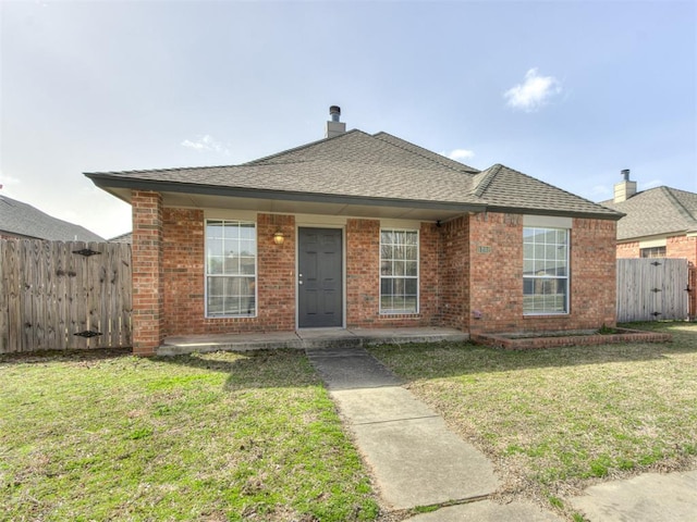 view of front of property featuring a front yard, fence, brick siding, and a shingled roof