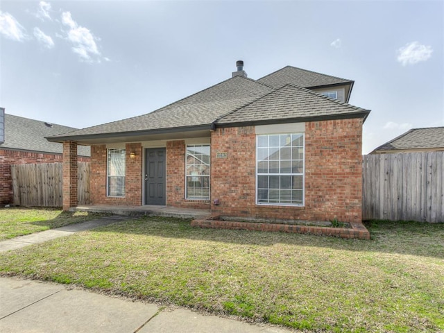 view of front of house featuring a front yard, fence, brick siding, and a shingled roof