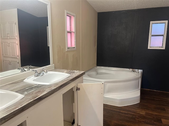 full bathroom with a wealth of natural light, a sink, a textured ceiling, and a bath