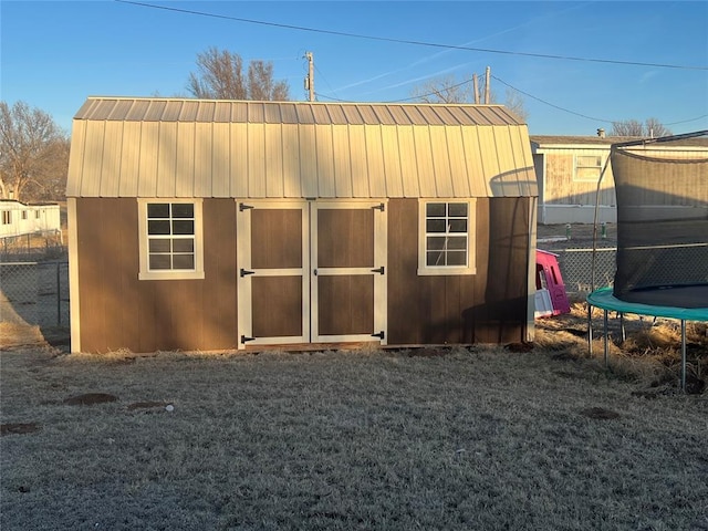 view of outbuilding featuring a trampoline, fence, and an outdoor structure