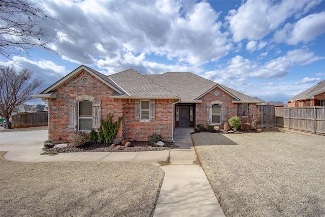 ranch-style home featuring roof with shingles, fence, and brick siding