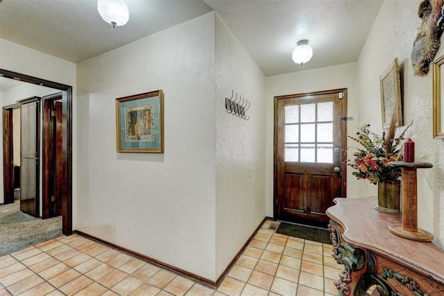 foyer entrance featuring light tile patterned floors, a textured ceiling, baseboards, and a textured wall